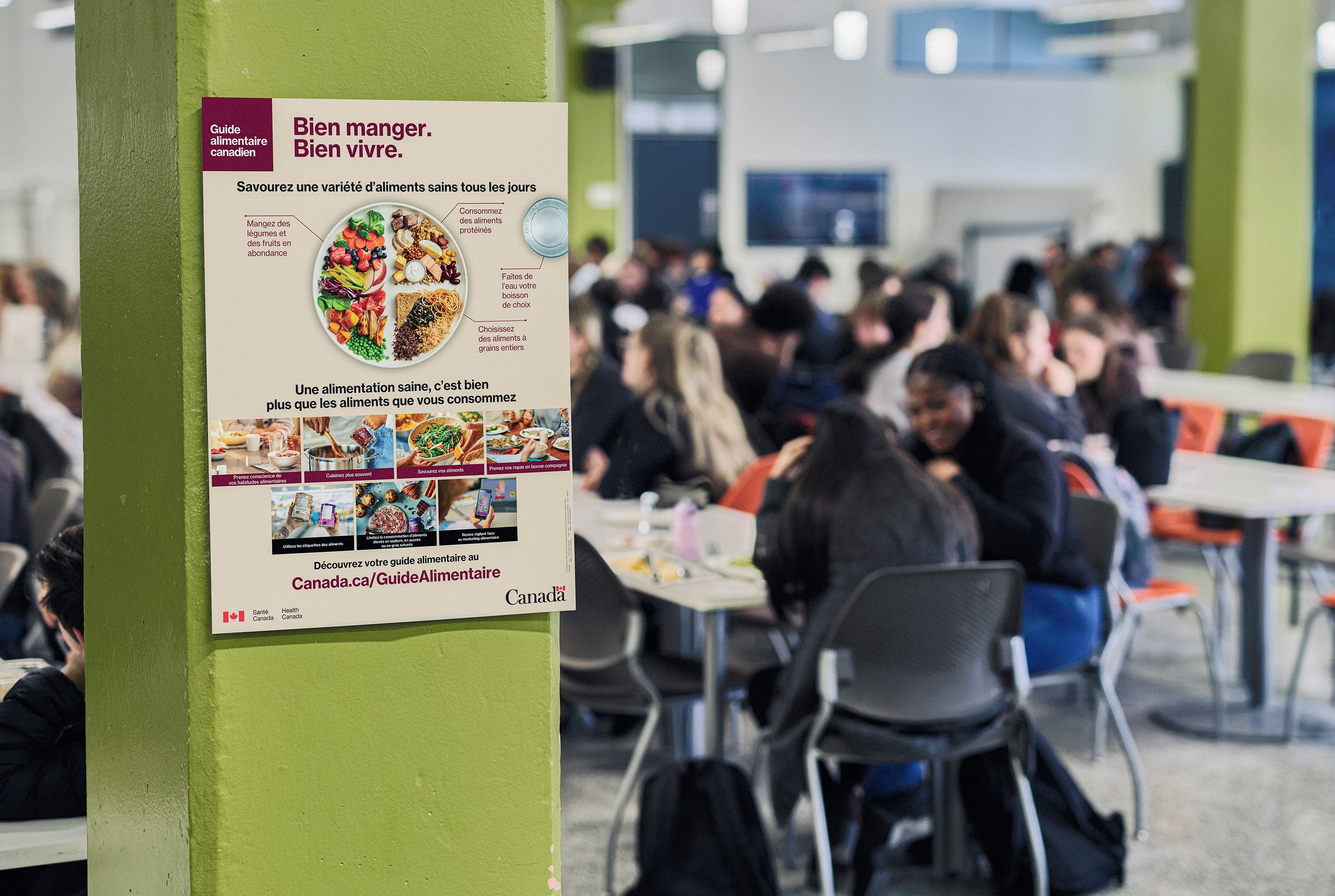 Deux étudiants sont assis dans une cafétéria remplie. Ils mangent leur repas et discutent ensemble, sans appareils électroniques ni autres distractions.