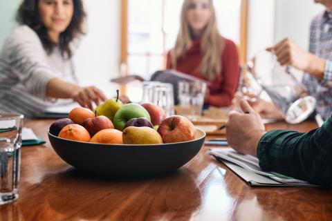 Bol de fruits mélangés sur la table, entourée d'un groupe de personnes.